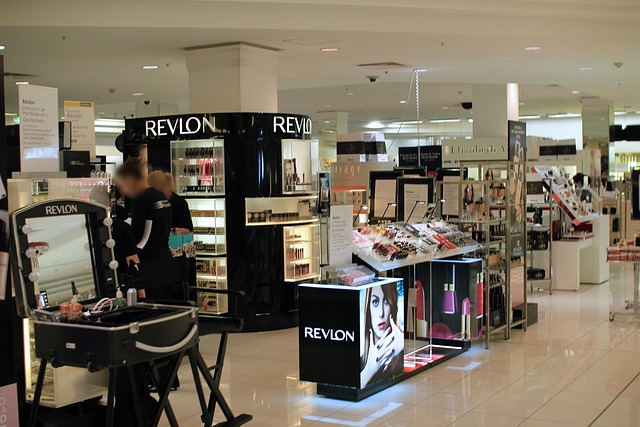 Отдел косметики Revlon в крупном универмаге с витринами, освещенными стендами и консультантами.
